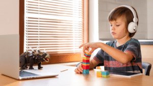Criança autista com fones de ouvido brincando com blocos coloridos enquanto assiste algo em um laptop.