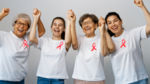 Pessoas em um centro comunitário de condomínio discutindo materiais de conscientização sobre câncer de mama com laços rosa.